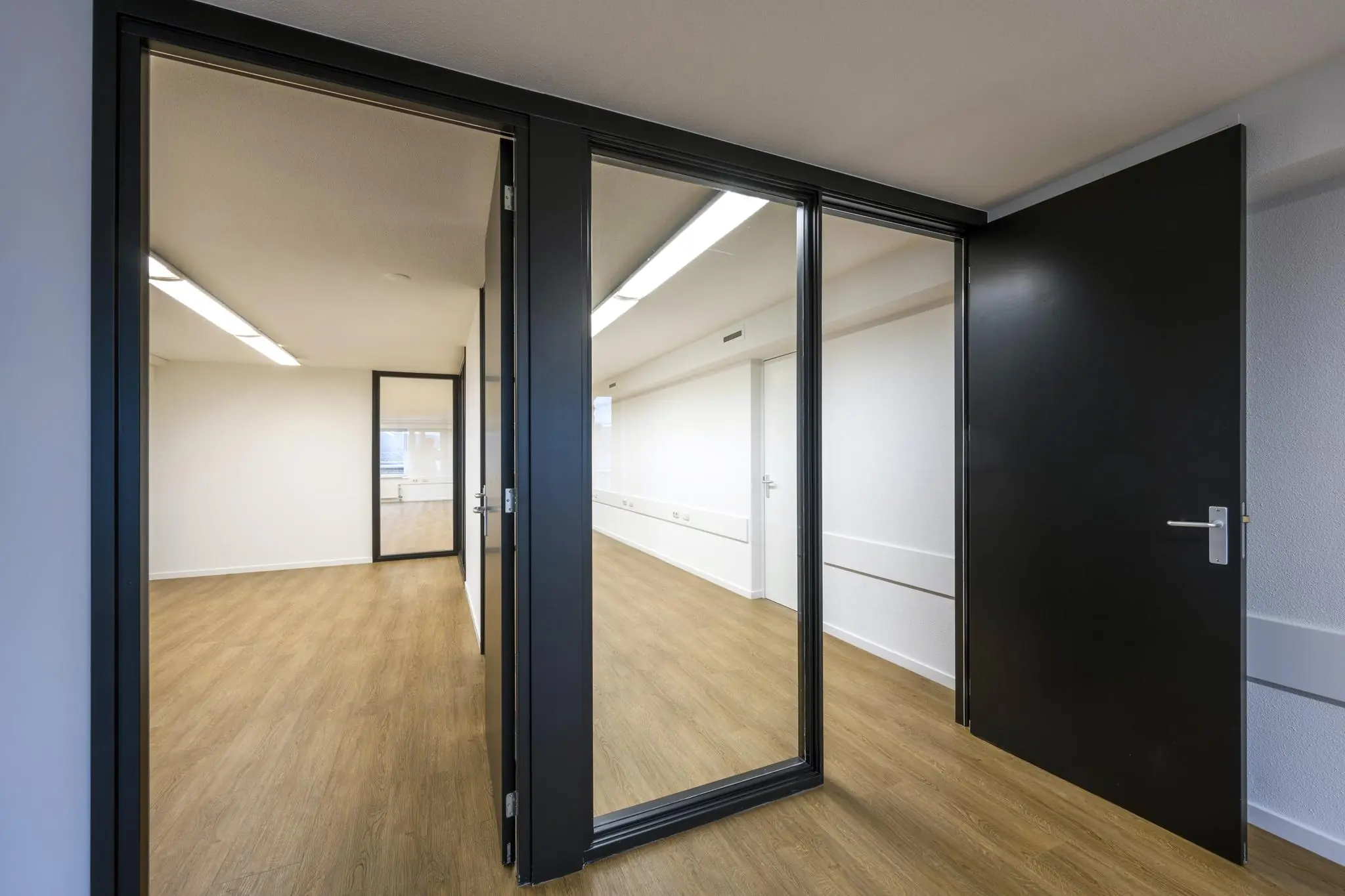 Moderne, lege kantoorruimte aan de Prins Hendrikkade met glazen wanden, houten vloer en zwarte deuren.